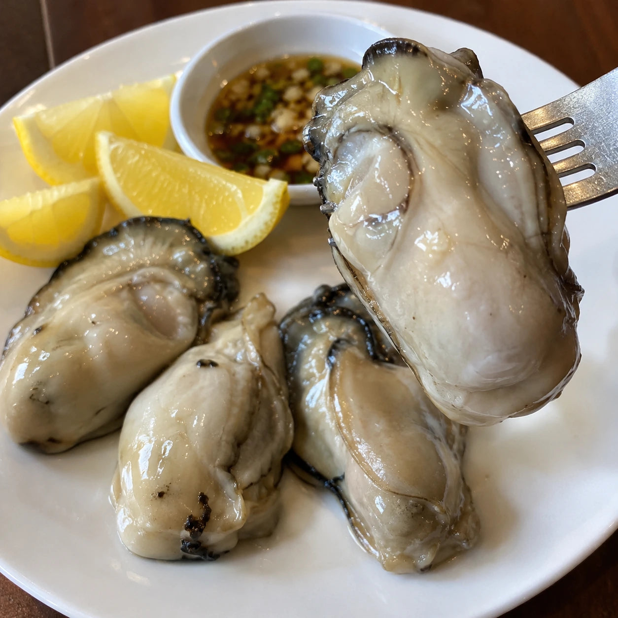Oysters on a white plate with lemon and dipping sauce.